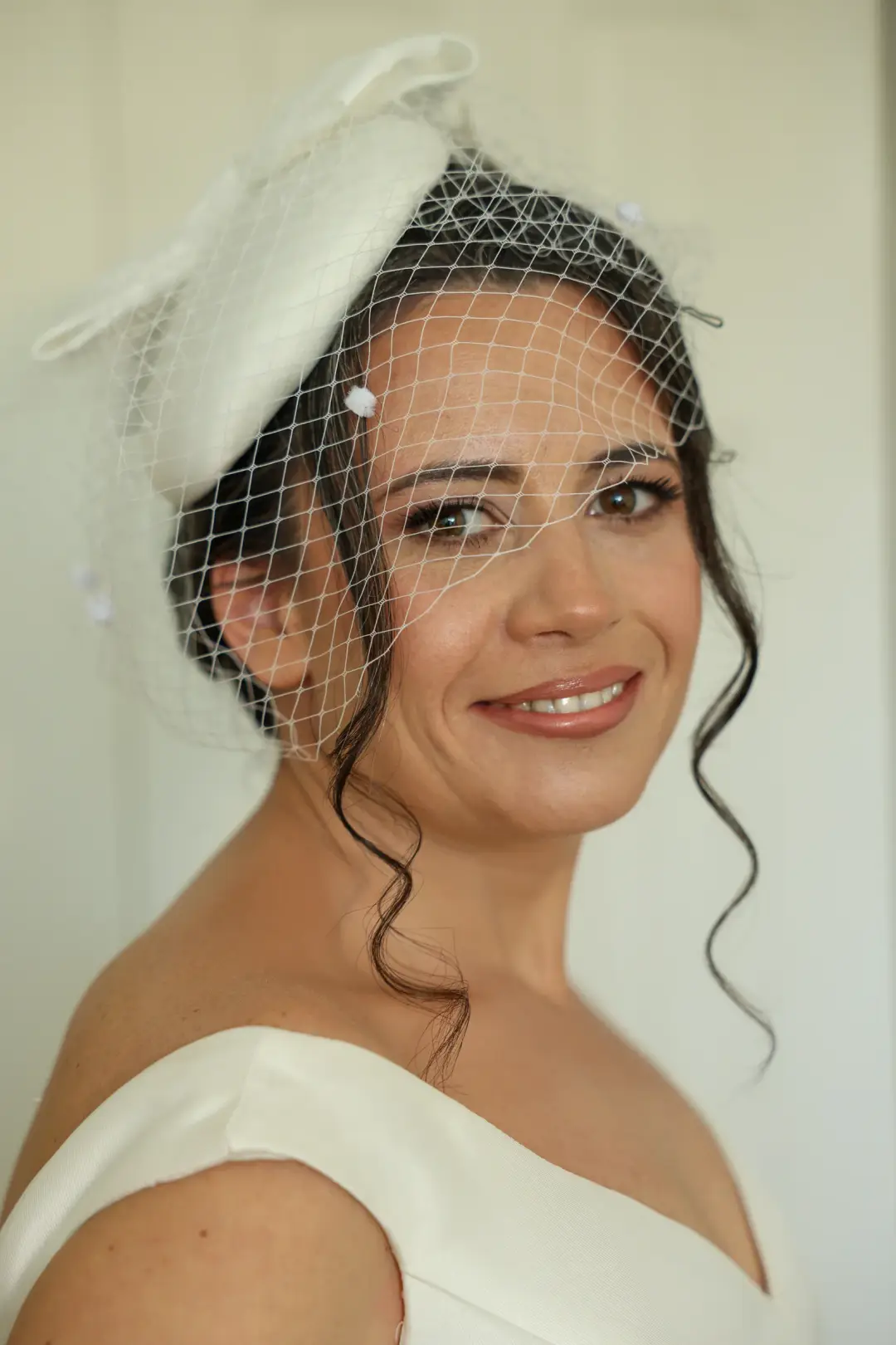 Bride with a dark updo, loose tendrils, and an ivory birdcage veil