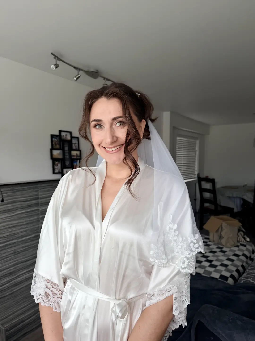 Bride in a white robe with a loose low updo, tendrils, and a veil
