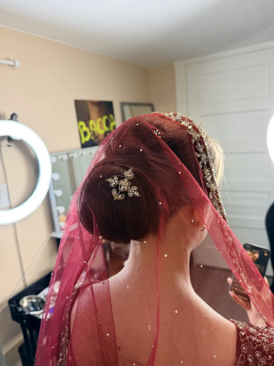 Smooth low bridal bun beneath a burgundy embellished veil
