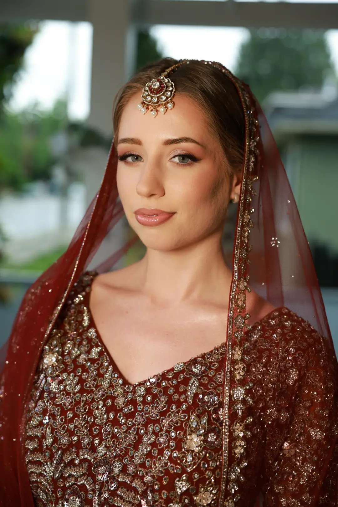 Bride in deep red with sleek centre-parted hair, a jeweled headpiece, and luminous makeup
