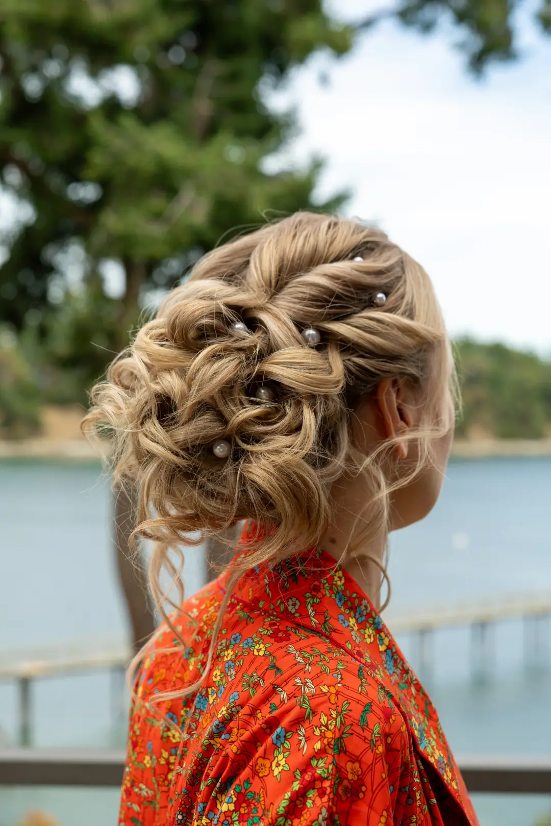 Intricate blonde low updo with twisted loops and pearl pins outdoors