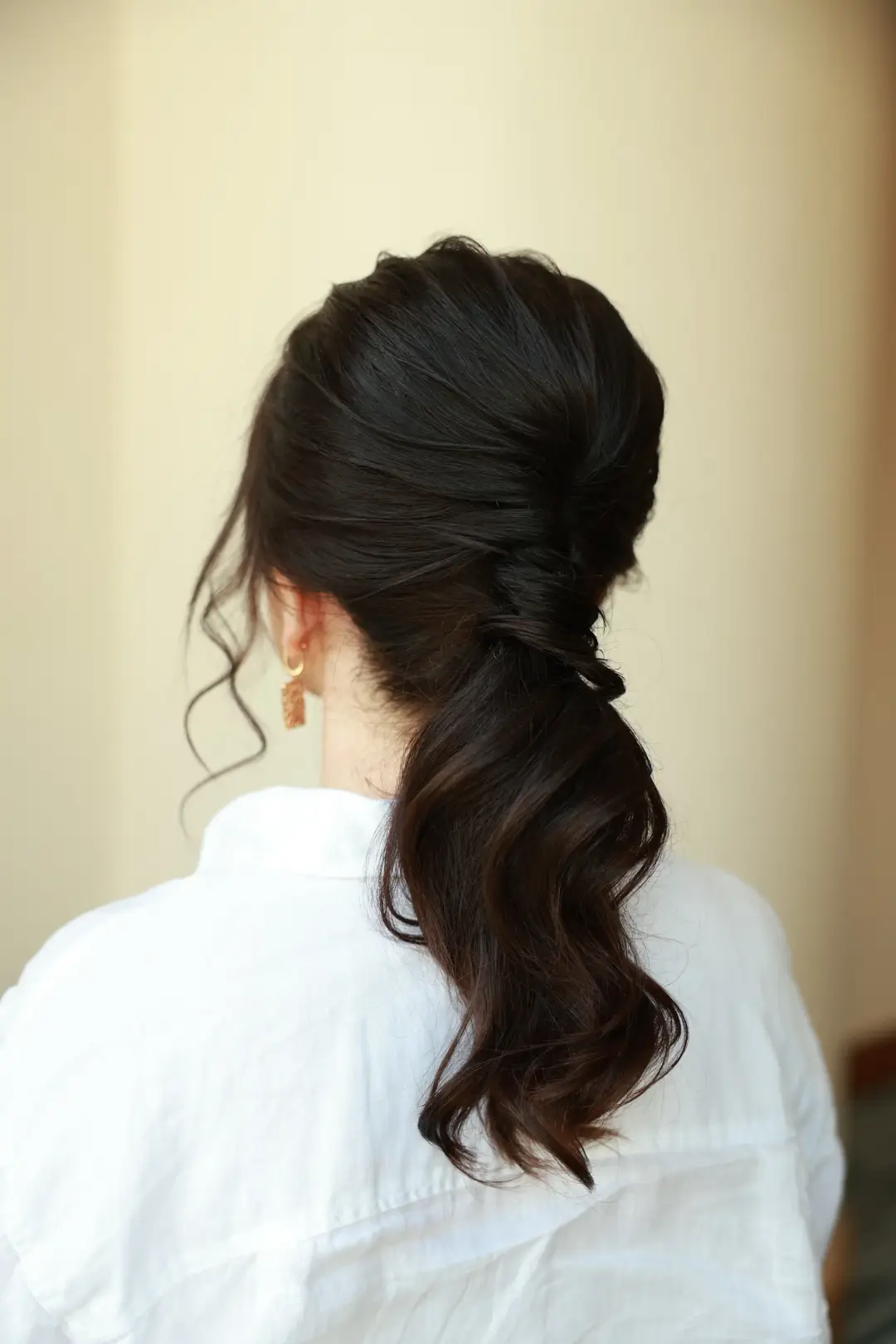Dark low ponytail with a smooth crown and soft face-framing curl