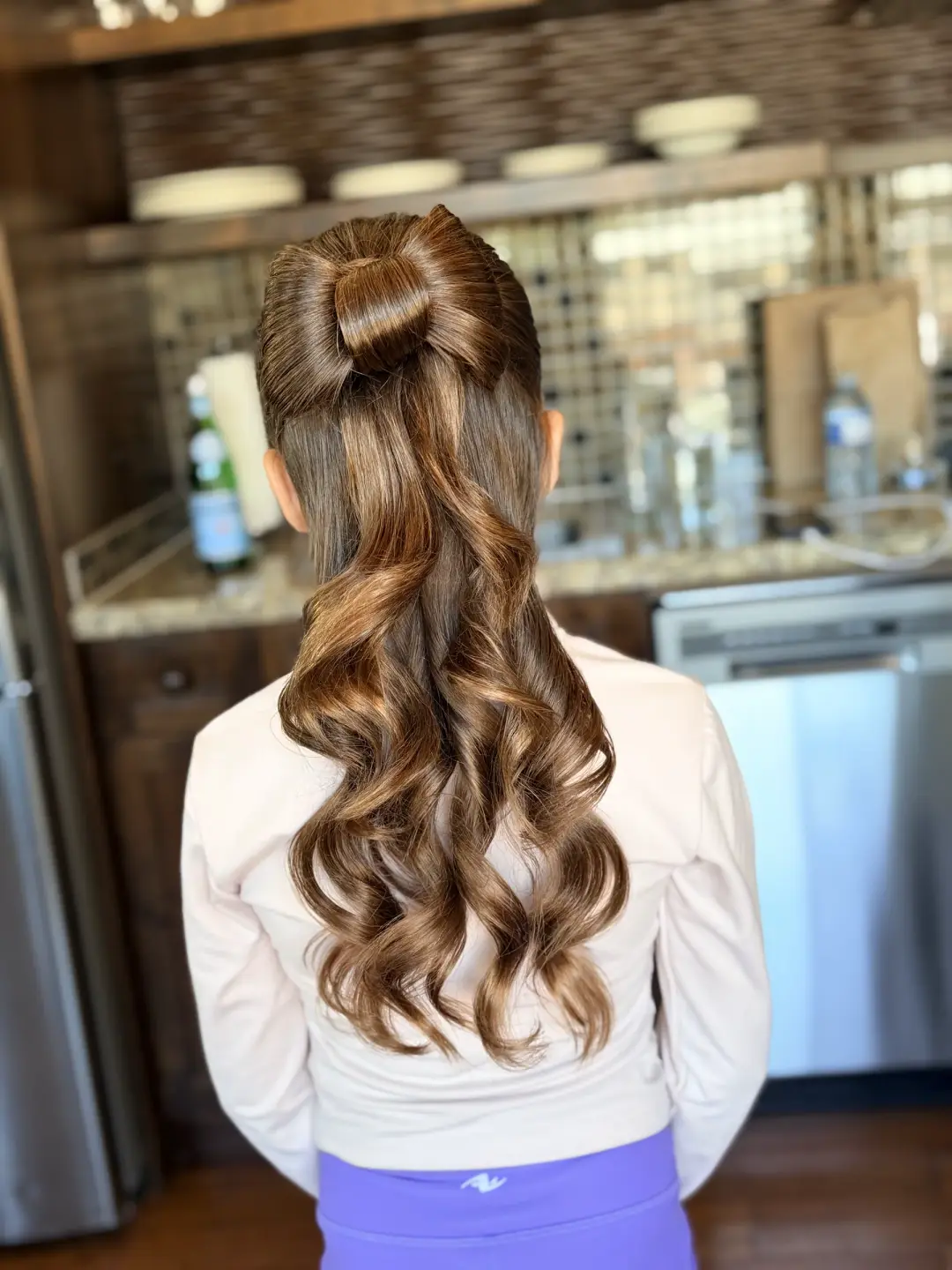High brunette ponytail with a knotted hair bow and polished curls