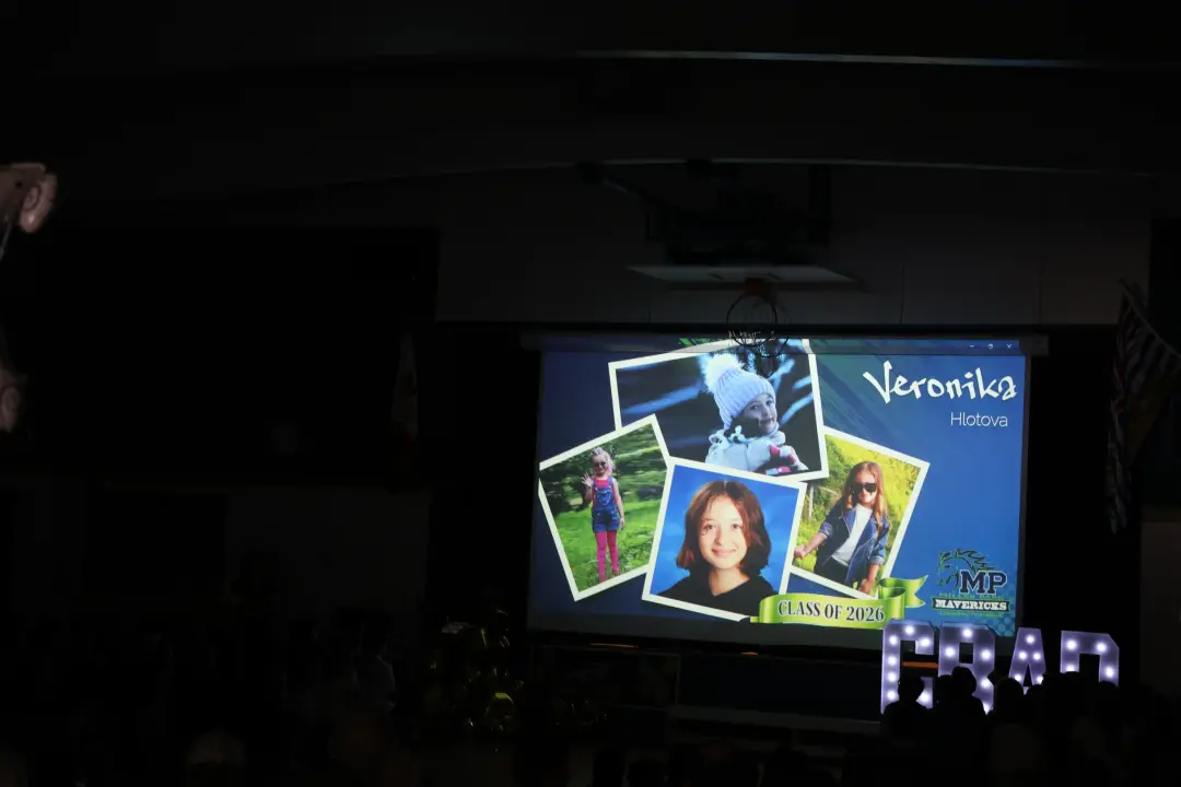 A slideshow collage lights up a school gymnasium screen during a graduation celebration, with glowing marquee letters below.