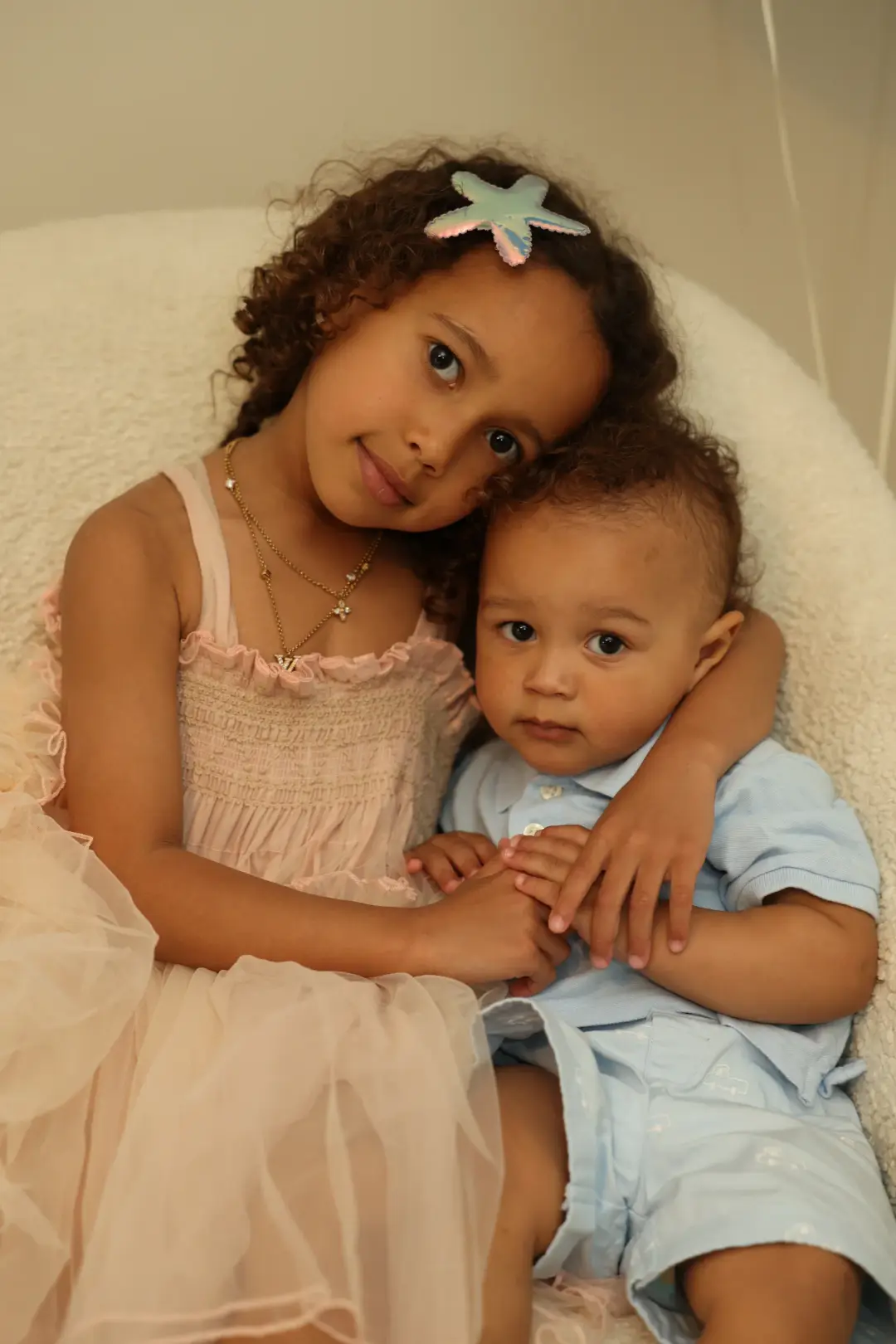 A young girl cuddles her baby brother on a soft blanket, both gazing at the camera during a family photo session.