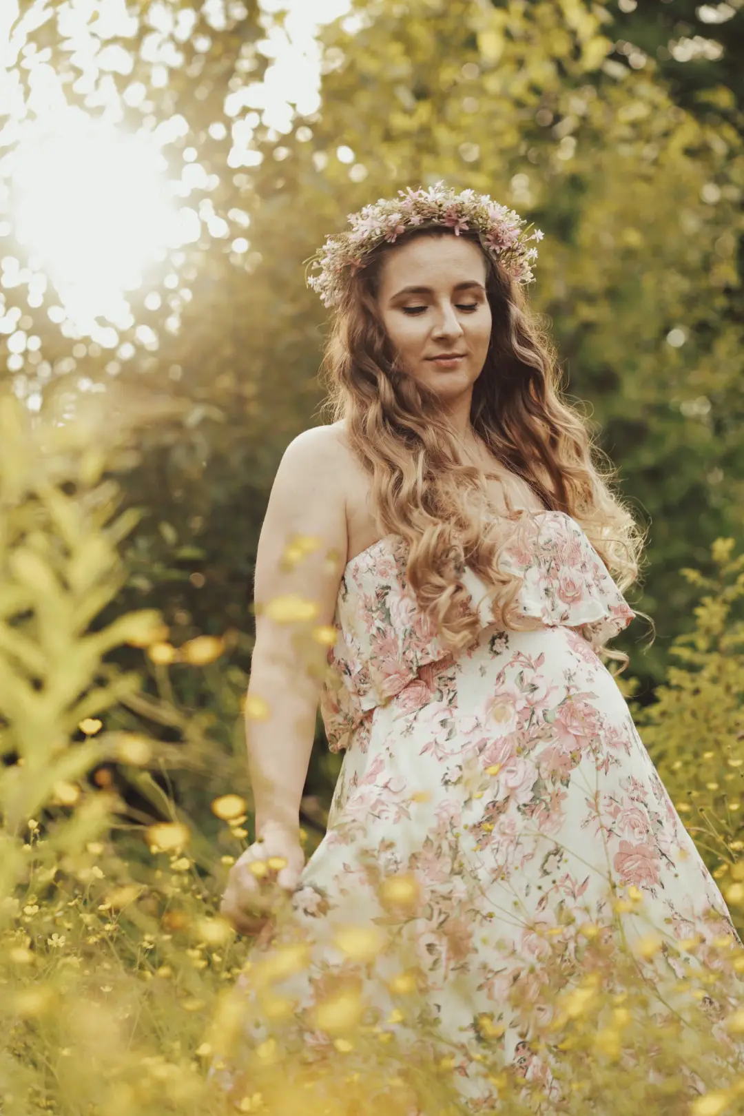An expectant mother in a flower crown standing serenely in golden evening light.