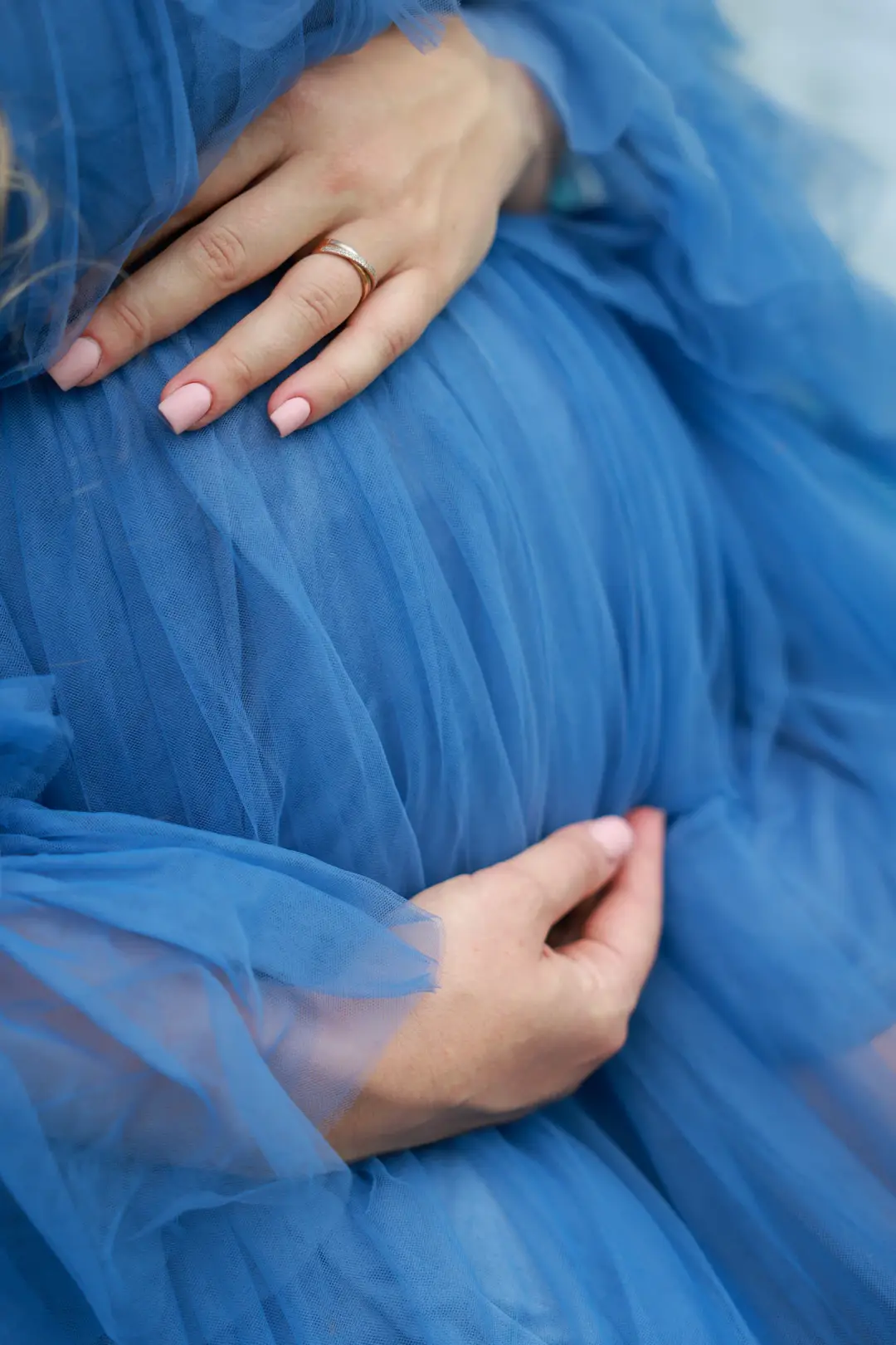 A close-up of hands resting on a pregnant belly draped in blue tulle.