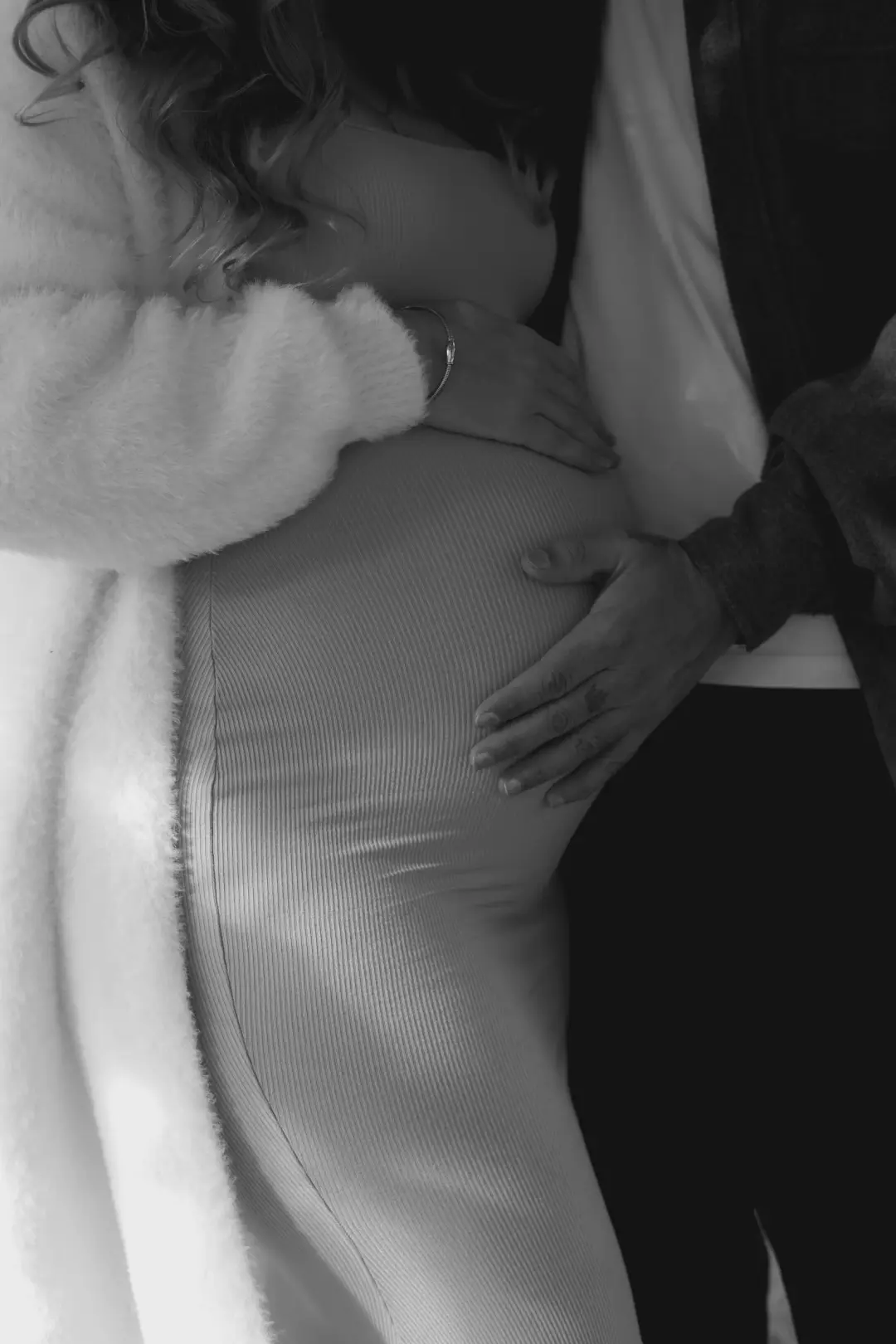 A black-and-white close-up of two hands resting together on a pregnant belly.