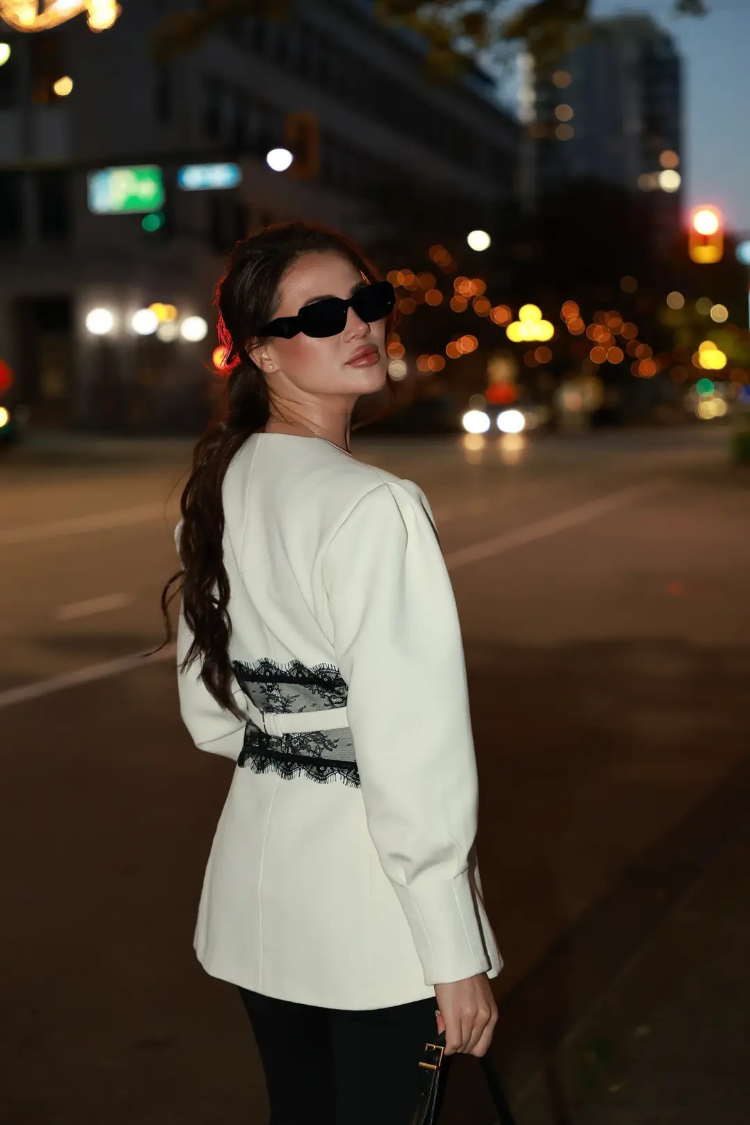 Nighttime portrait of a woman in a white blazer glancing over her shoulder on a city street lit by traffic lights