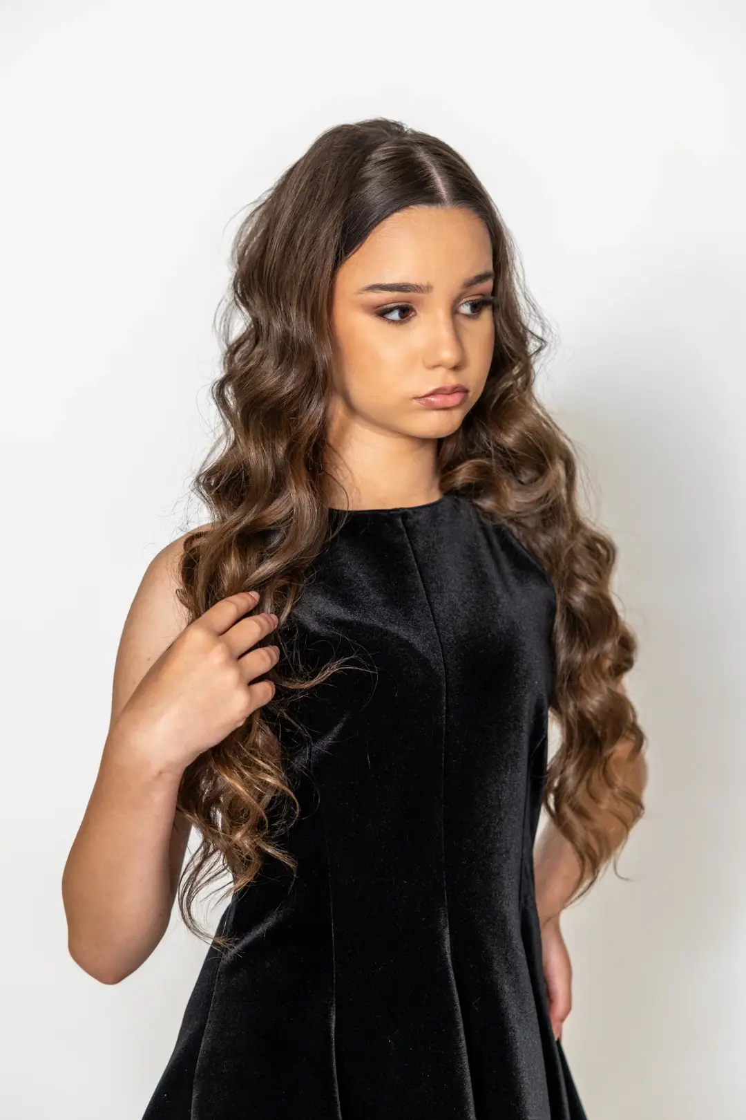 Studio portrait of a young woman in a black velvet dress, gently touching a strand of her hair