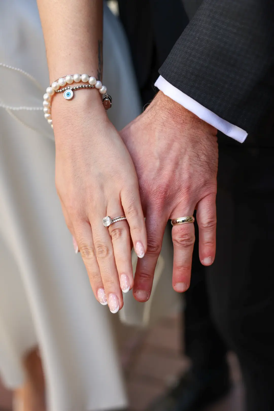A close view of the couple's joined hands showing their wedding and engagement rings.