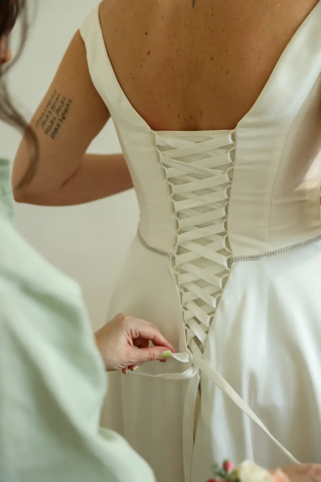A close view of the corset-laced back of the wedding gown being tied by hand.