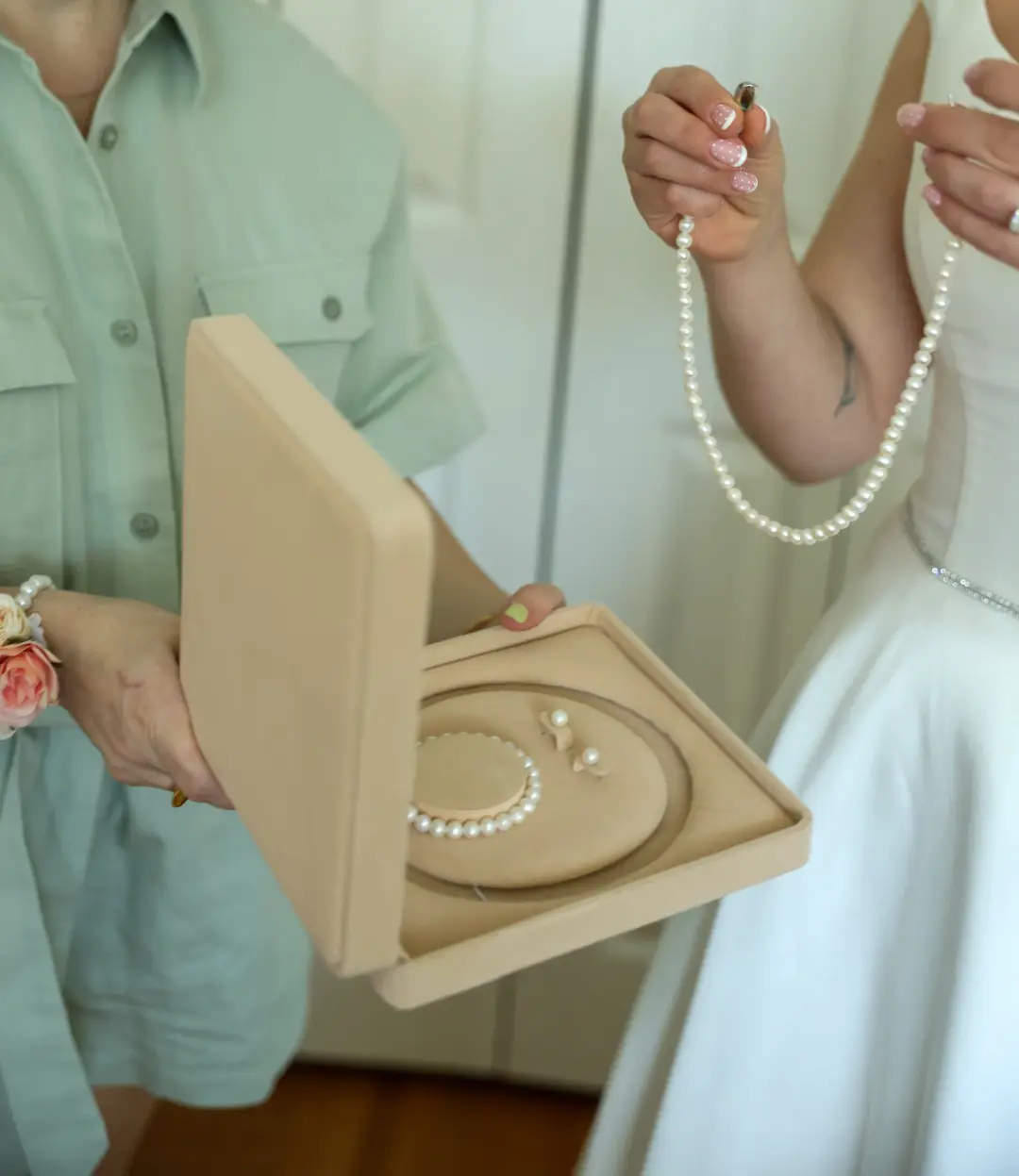 A woman opening a jewelry box of pearls while the bride holds up a pearl necklace.