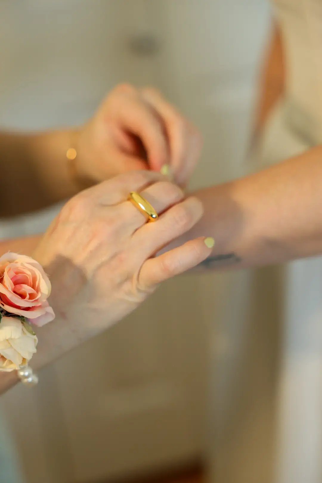 A close view of hands adjusting a ring, with a rose wrist corsage nearby.