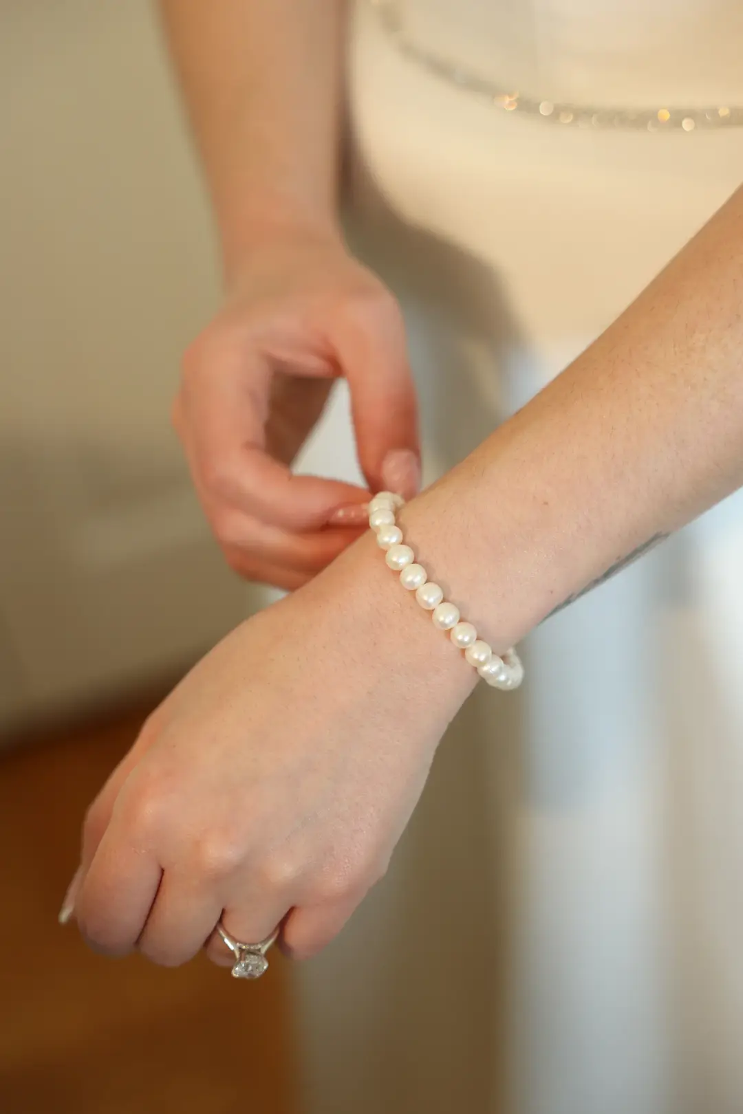 A close-up of the bride's wrist as a pearl bracelet is fastened, her engagement ring in view.