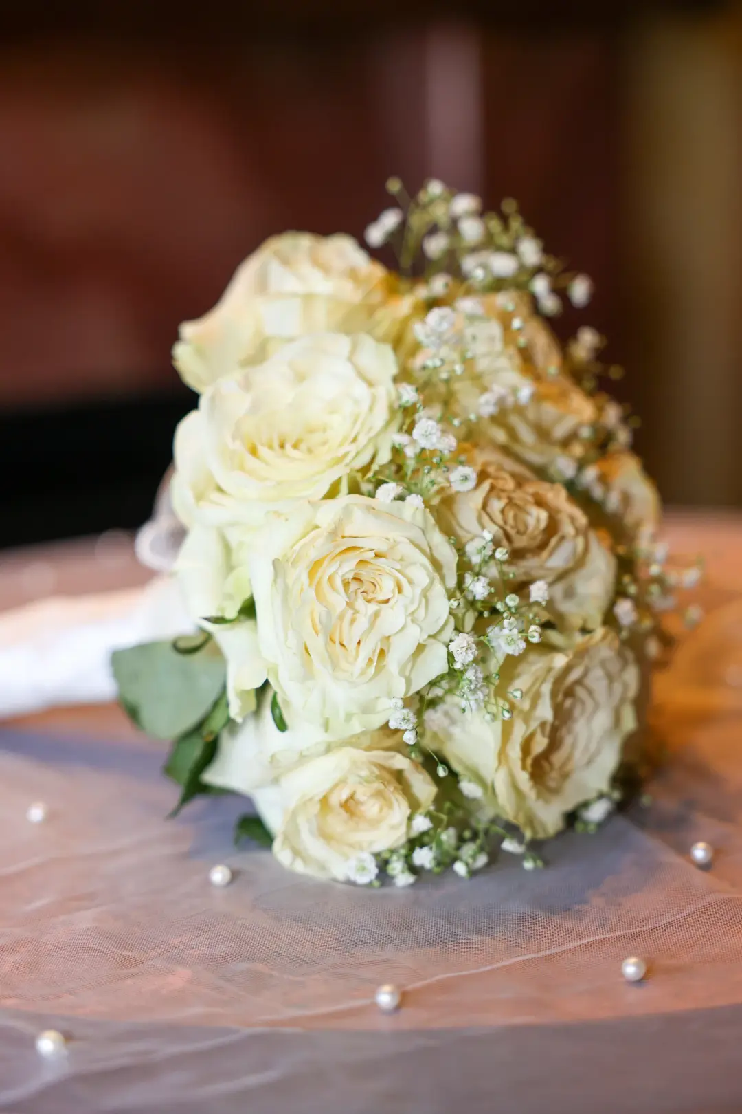A bridal bouquet of white roses and baby's breath displayed on a table.