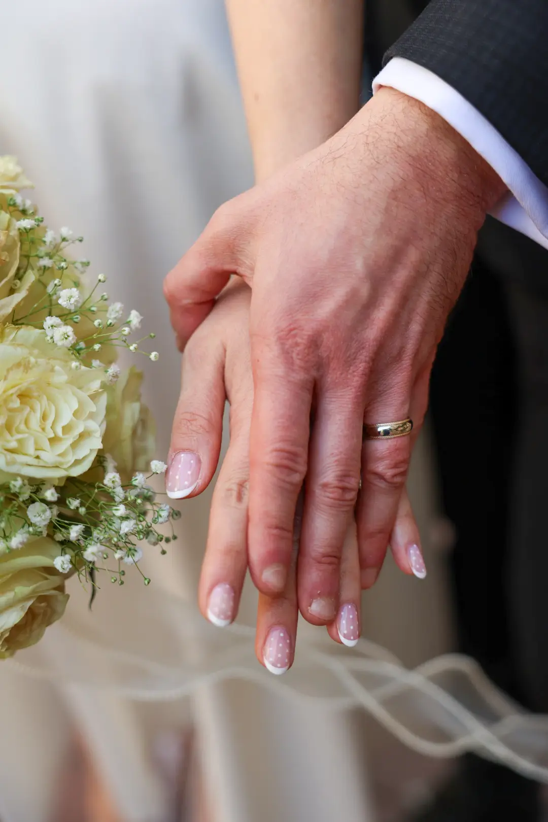 A close view of the couple's clasped hands over the bridal bouquet.