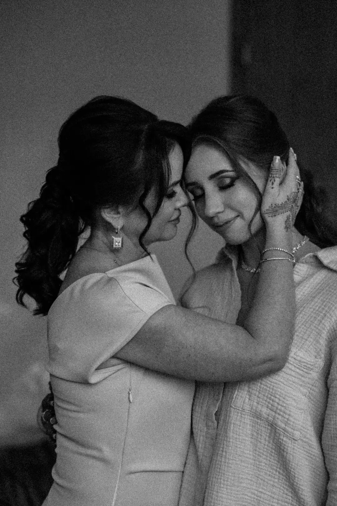 A black-and-white portrait of two women sharing a tender embrace, foreheads close together.