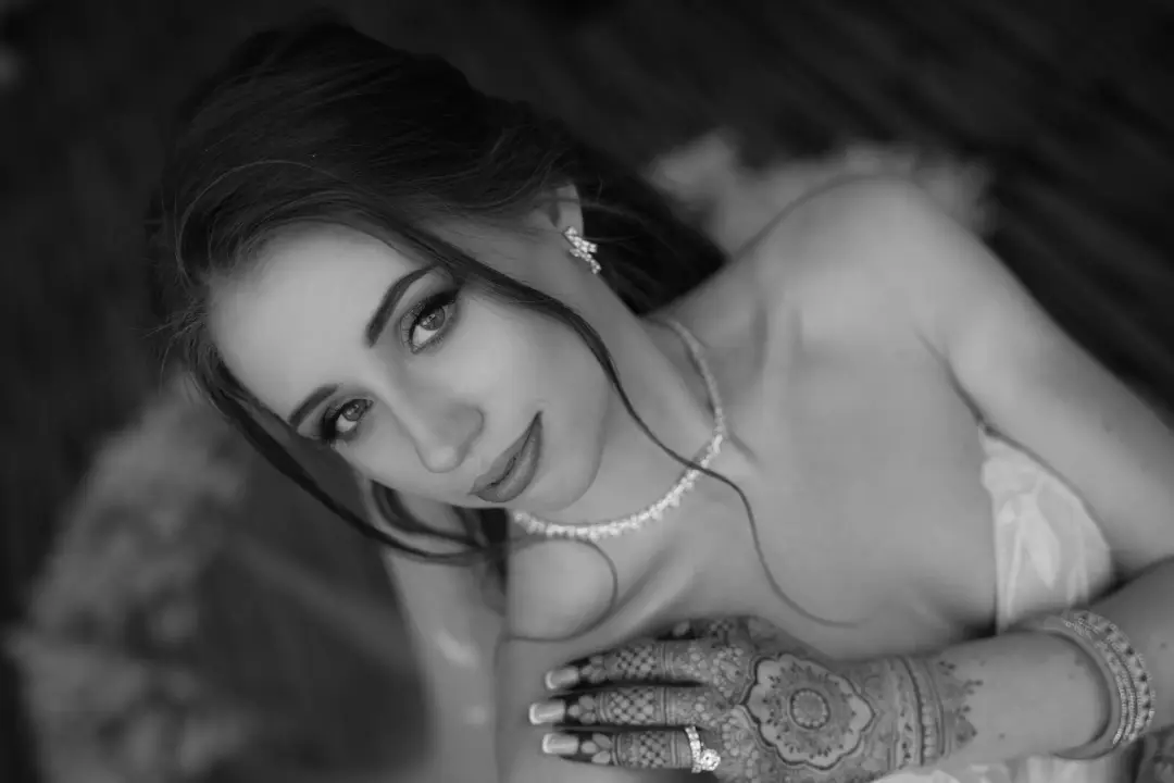 A black-and-white close-up portrait of the bride, her hand adorned with intricate henna resting on her shoulder.