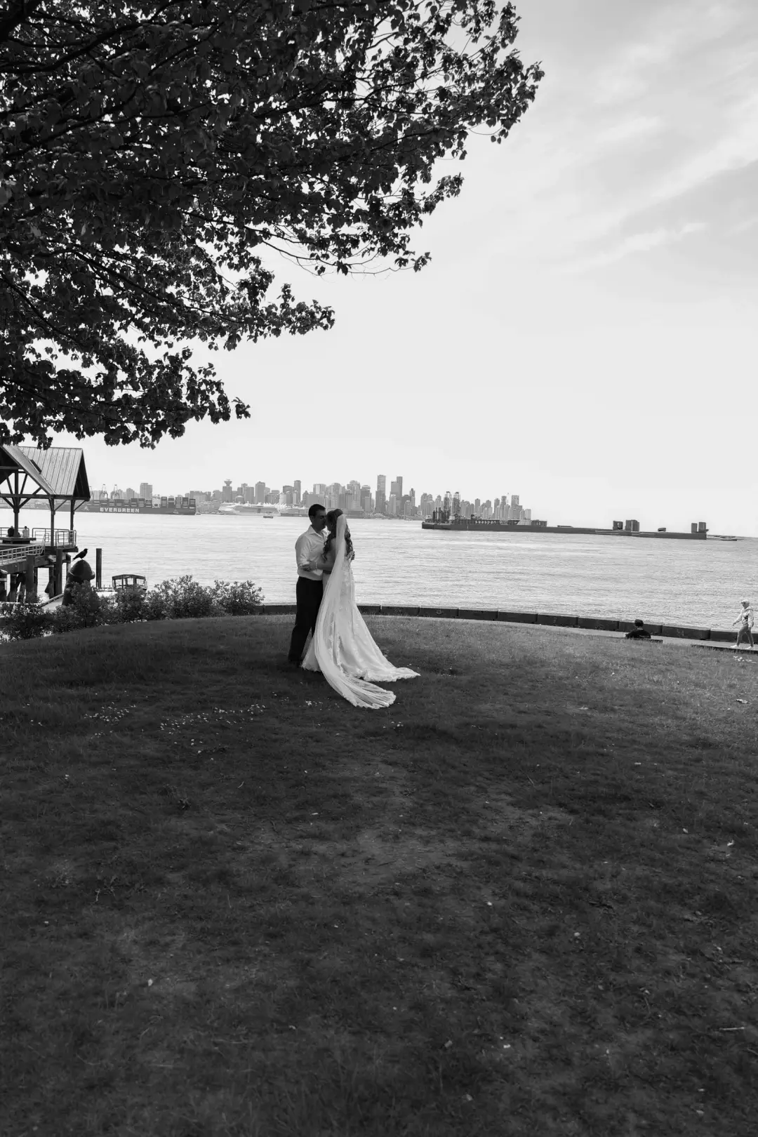 A black-and-white wide shot of the couple embracing on a grassy point overlooking the city skyline.