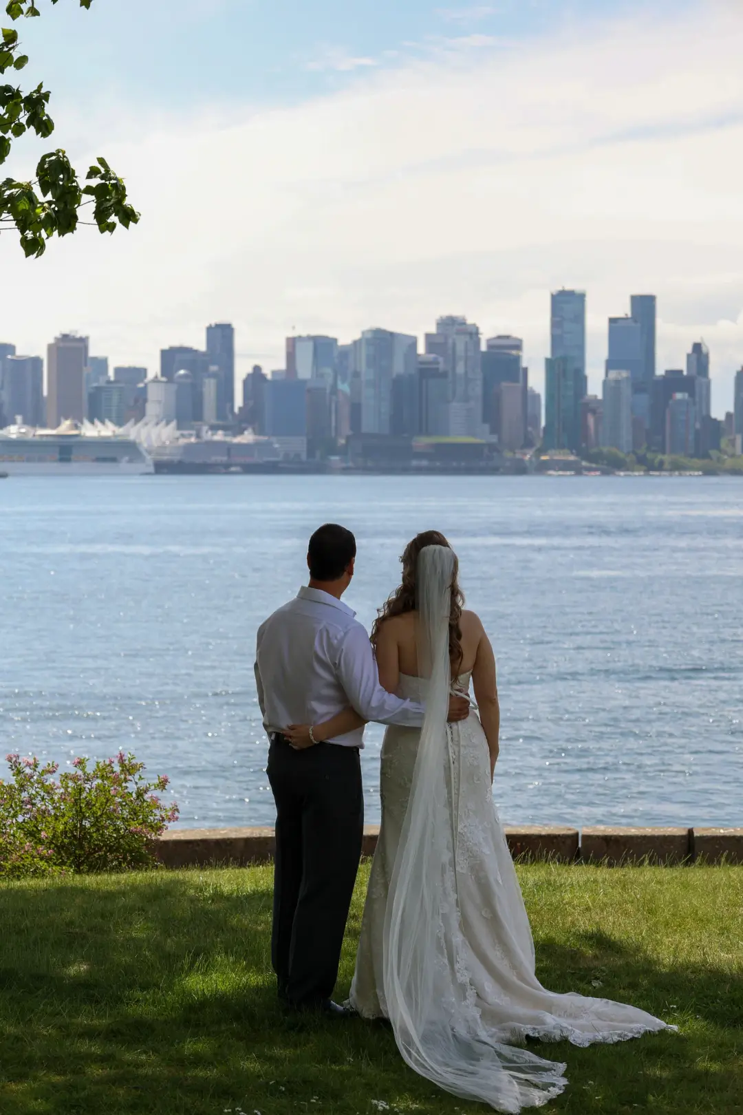 The couple standing arm in arm by the water, taking in the city skyline together.