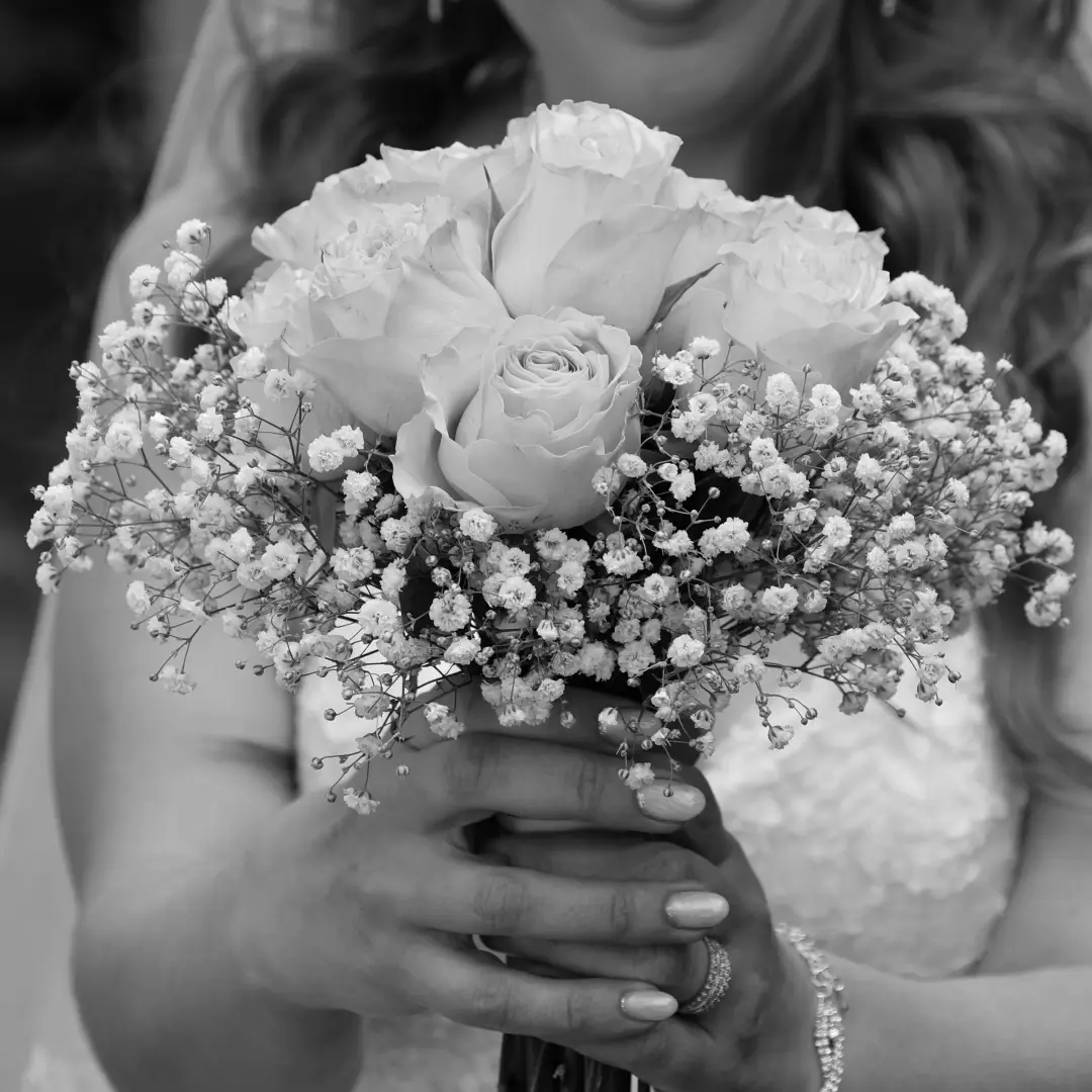 A black-and-white close-up of a bouquet of roses and baby's breath held in hand.