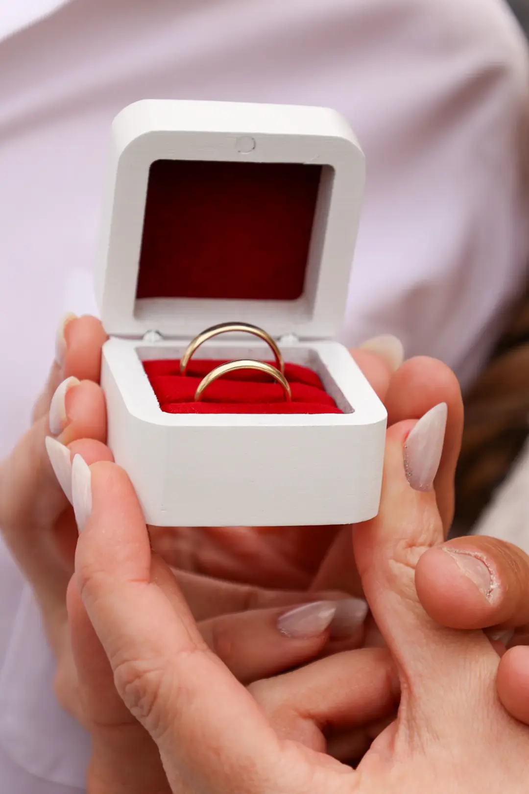 A small open ring box revealing two gold wedding bands on red velvet.