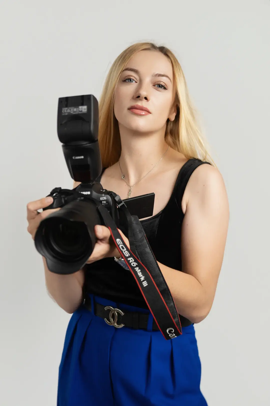 Raisa Hryhoriak holding a Canon camera with an external flash, wearing a black top and blue trousers.